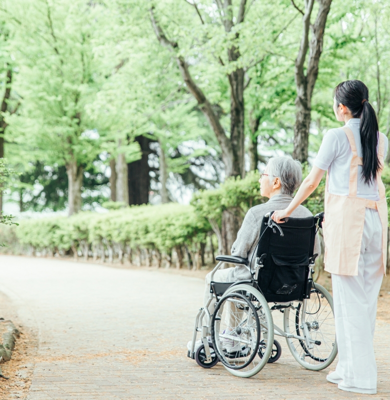 介護職員が車椅子利用者を緑豊かな散策路でサポート。